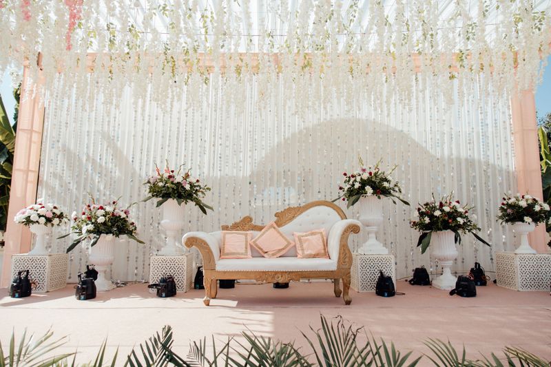 Ivory and blush stage with hanging florals and a gilded settee